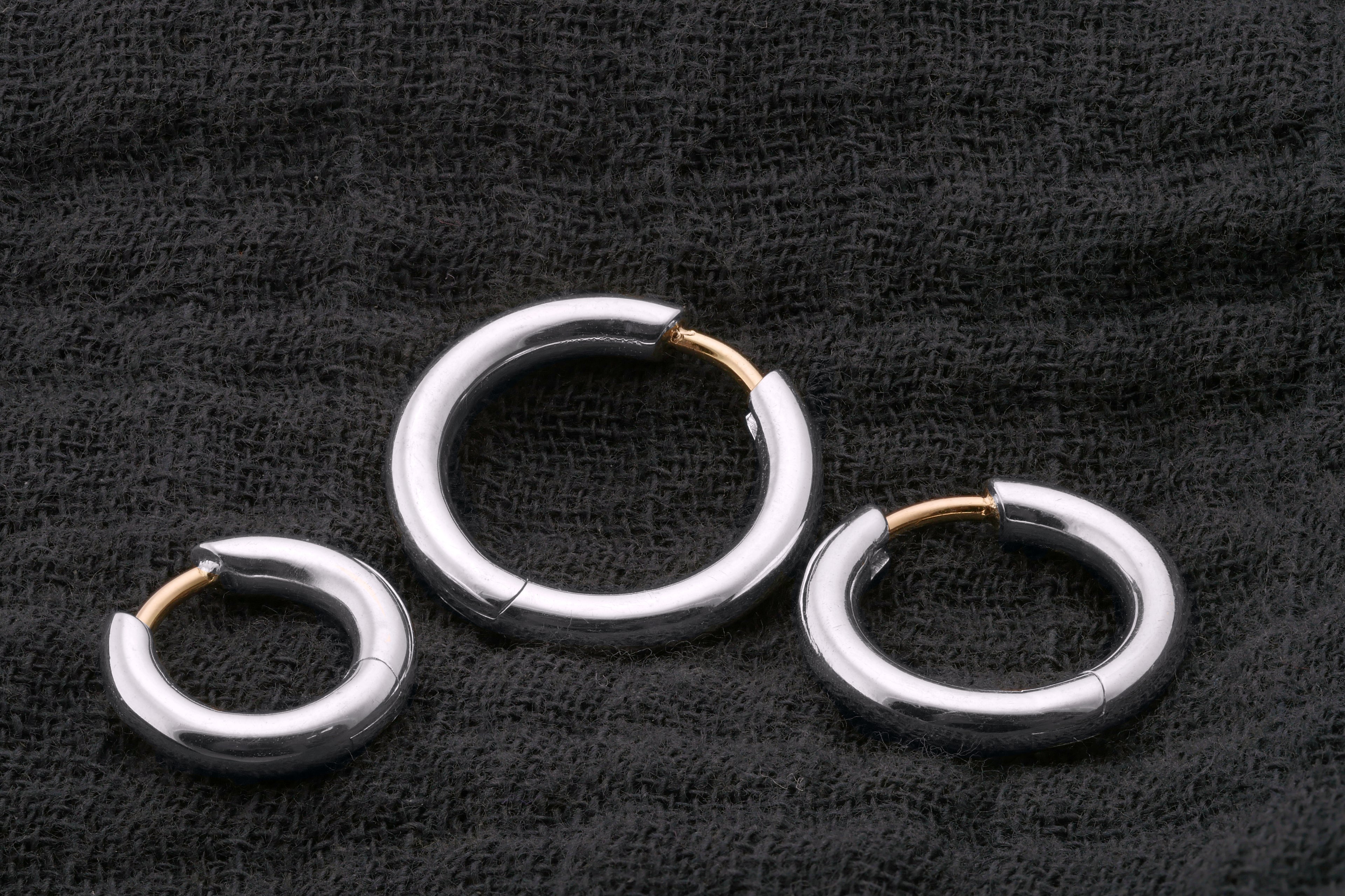 Three silver hoop earrings with gold accents on a black textured background