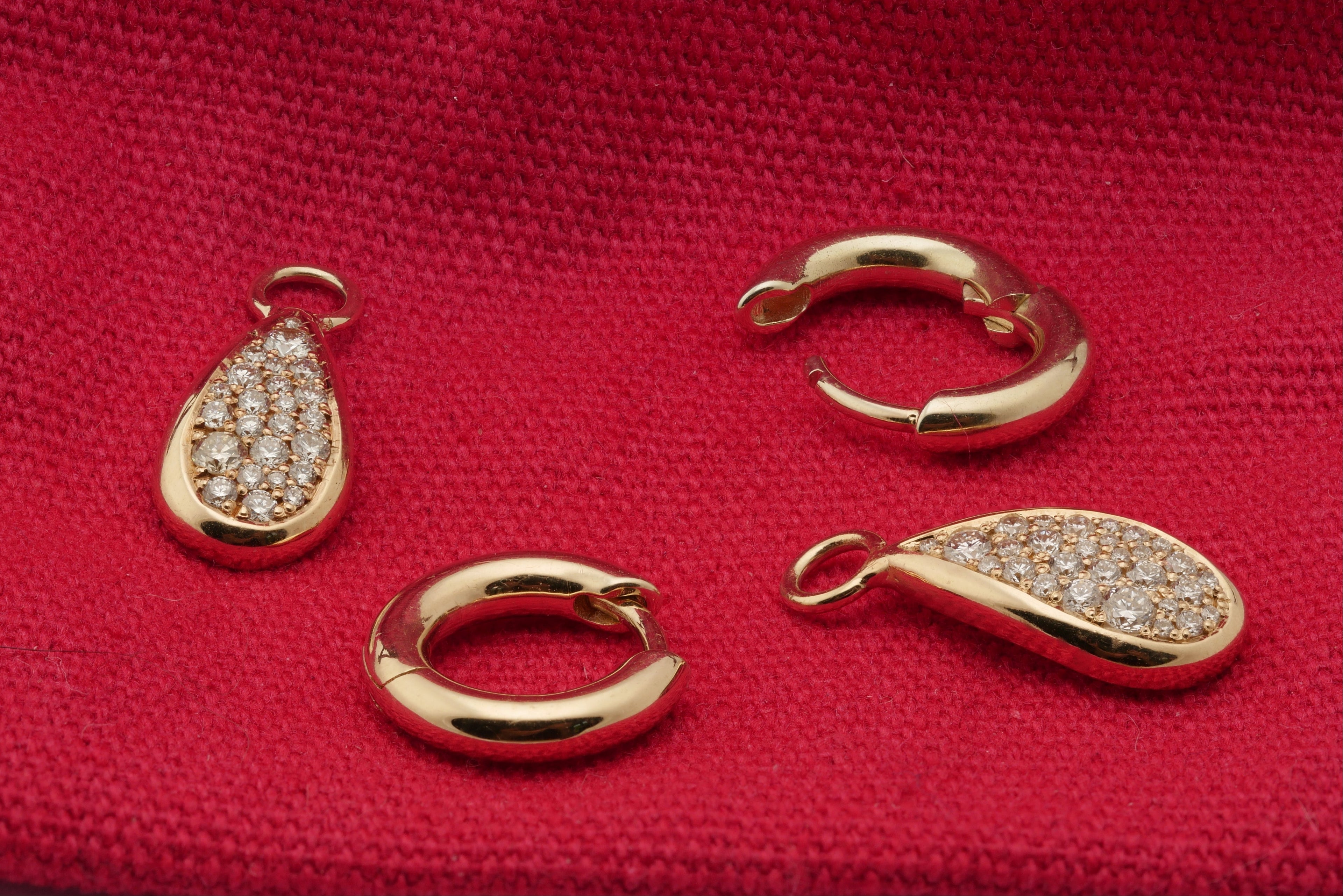 luxury Gold jewelry pieces including a diamond teardrop pendant and gold huggie hoop earrings on a red fabric background